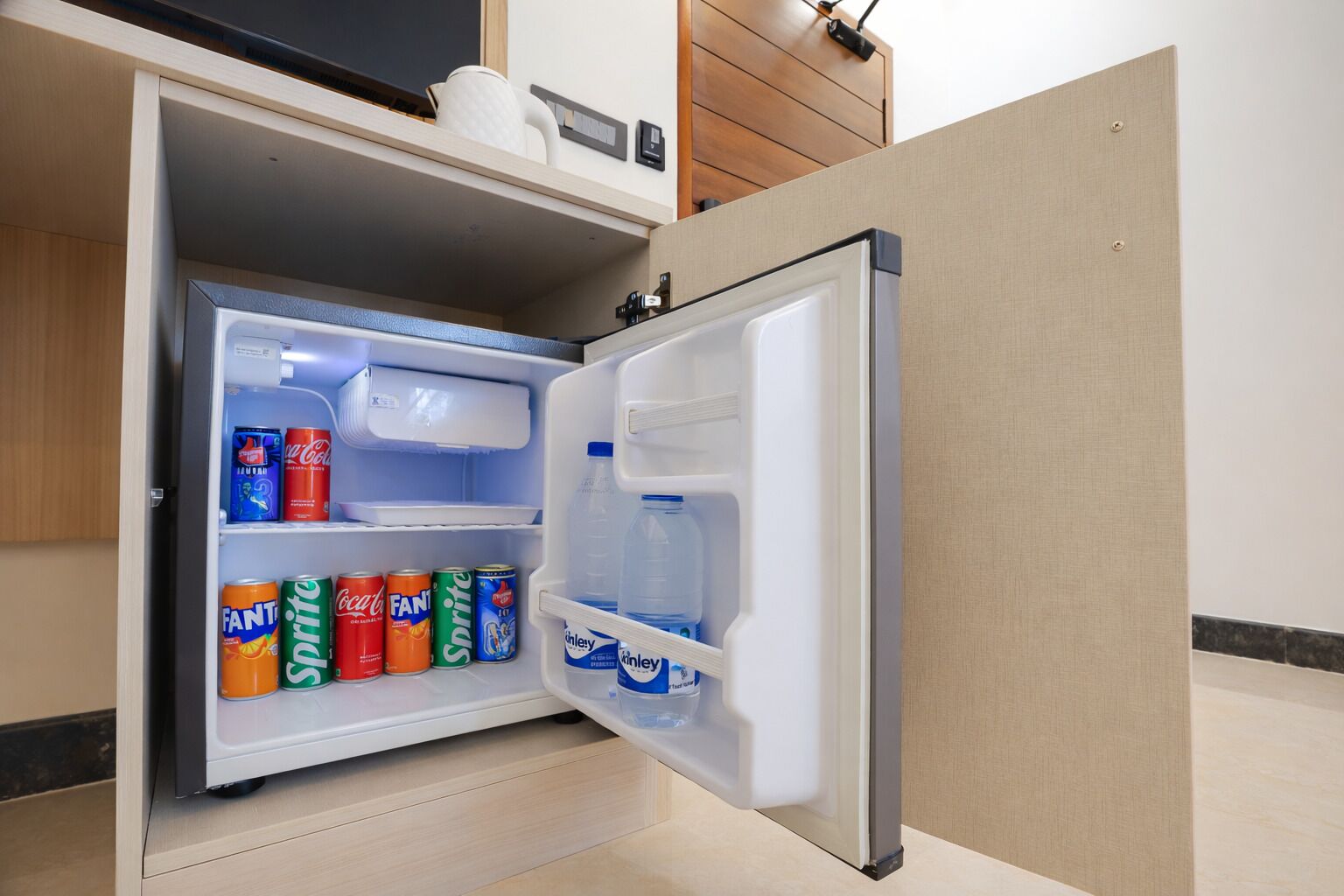 A compact refrigerator with a freezer compartment, containing beverages and a water bottle.