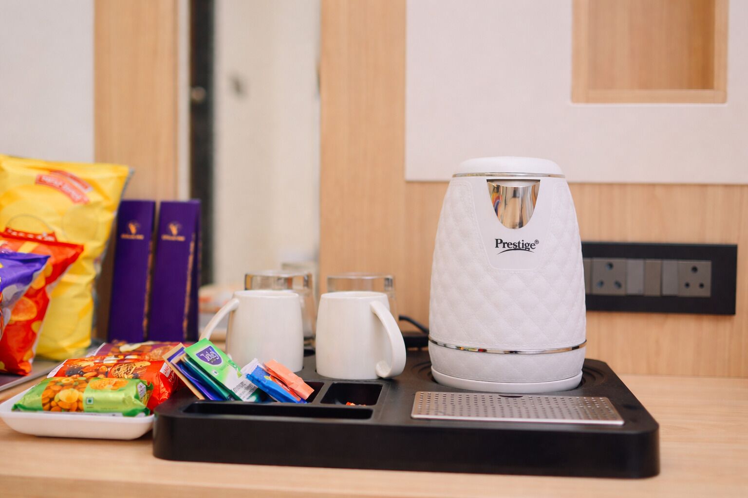 A coffee maker, a tray with snacks, and two cups on a table.
