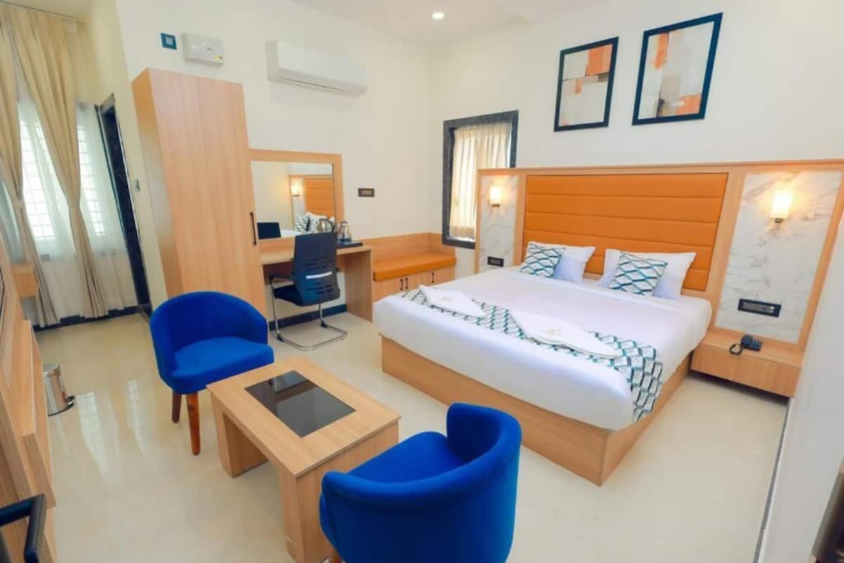 A hotel room with a bed, two blue chairs, a desk, a wardrobe, and a mirror.