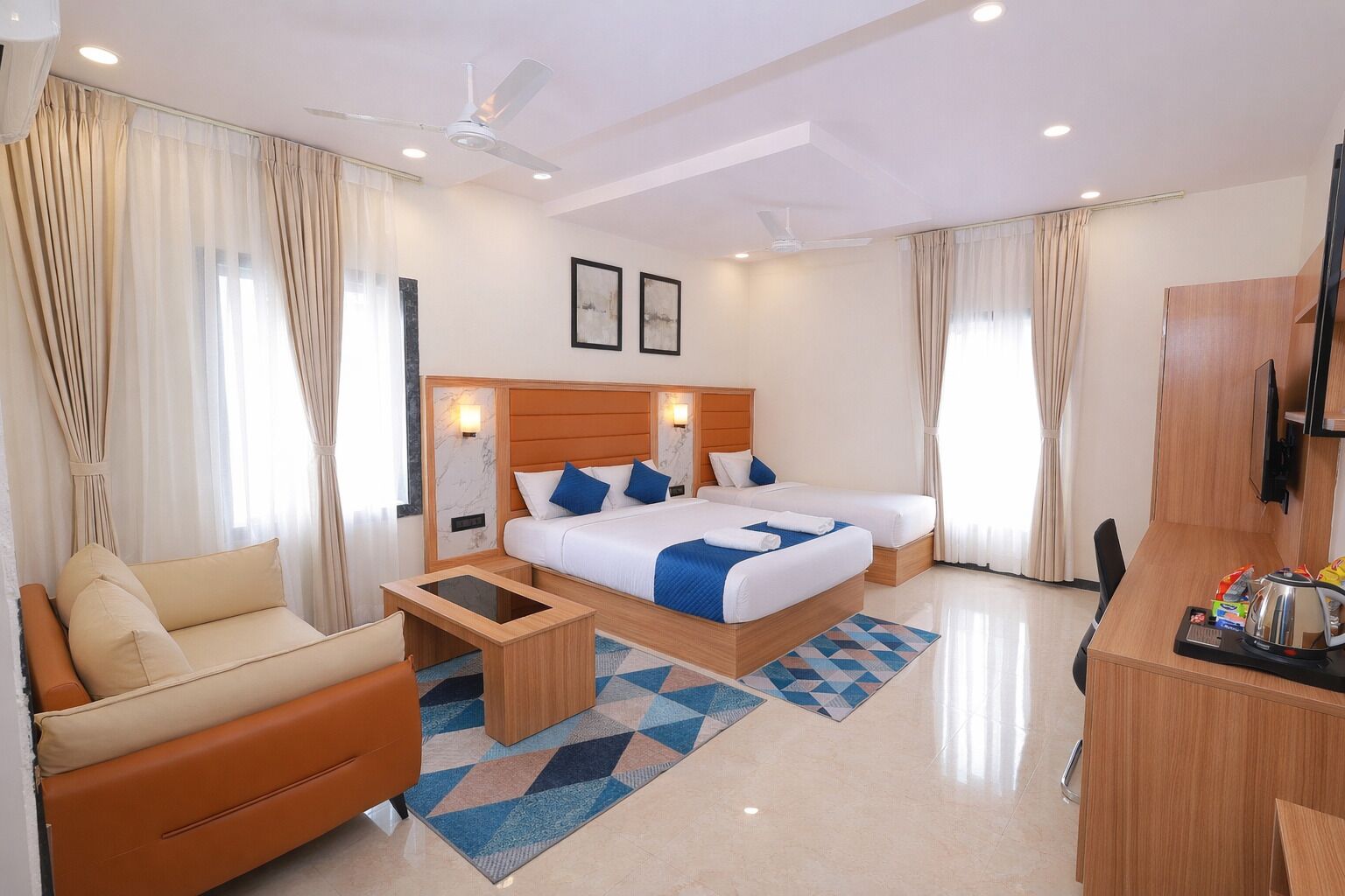 A hotel room with a bed, a sofa, a desk, a TV, and a ceiling fan.