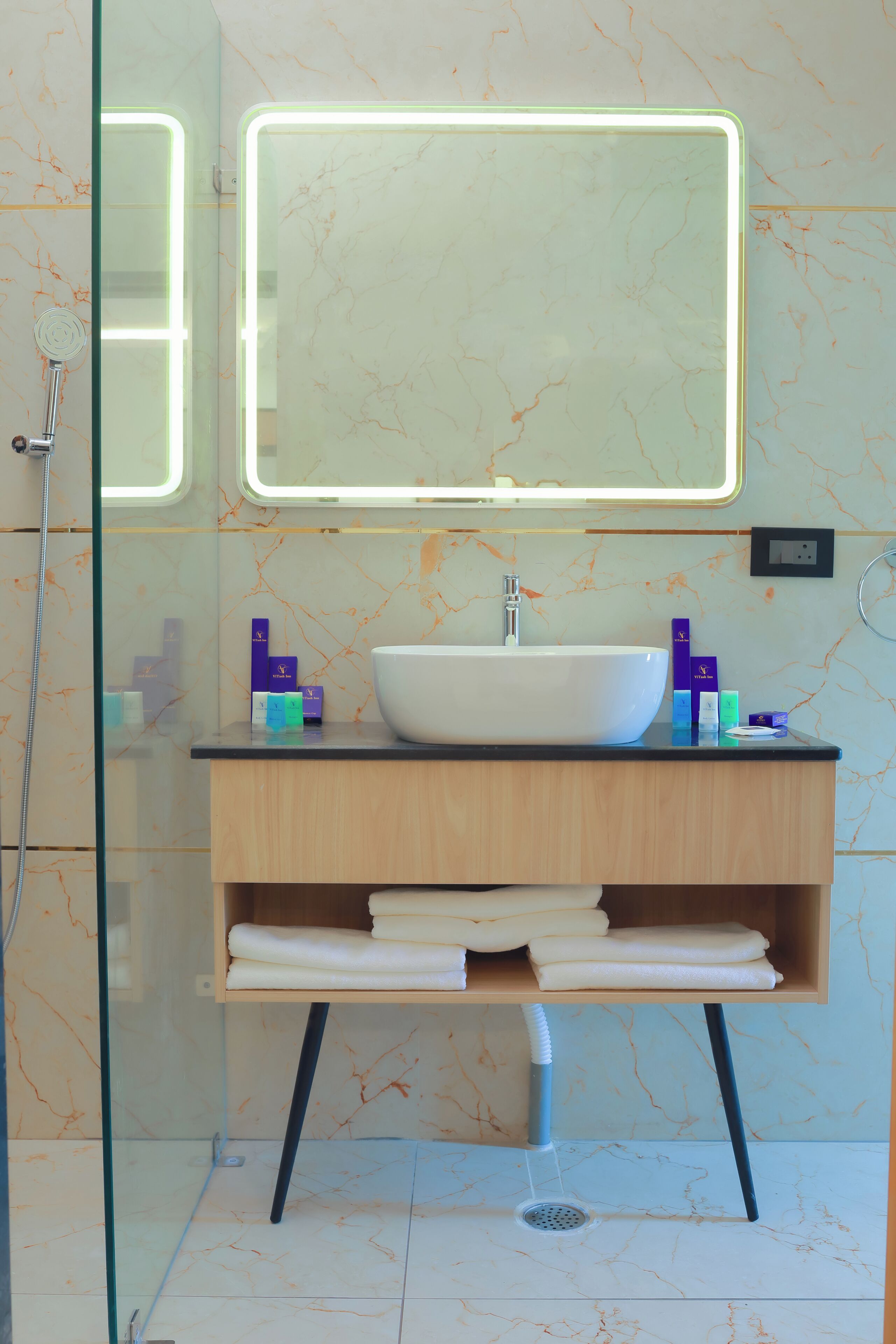 Un baño moderno con un lavamanos grande y blanco, un espejo con bordes iluminados y una cabina de ducha de vidrio.