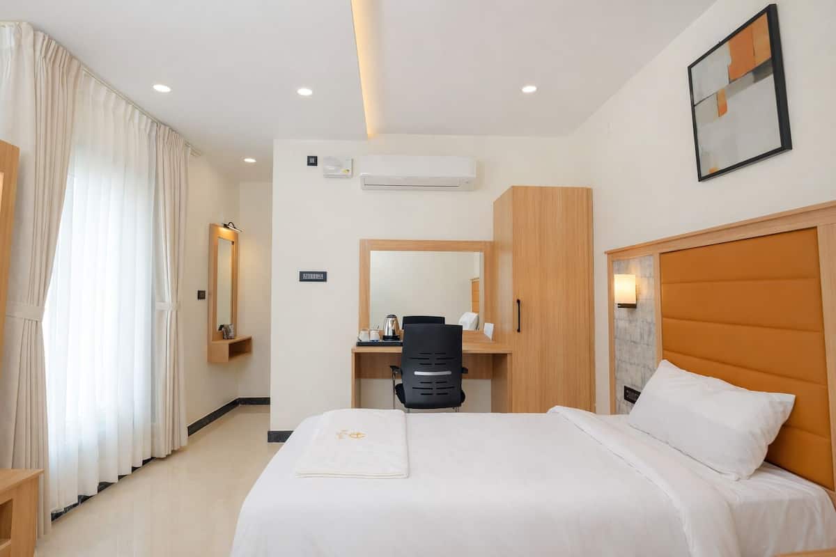 A hotel room with a bed, a desk, a chair, a wardrobe, and an air conditioning unit.