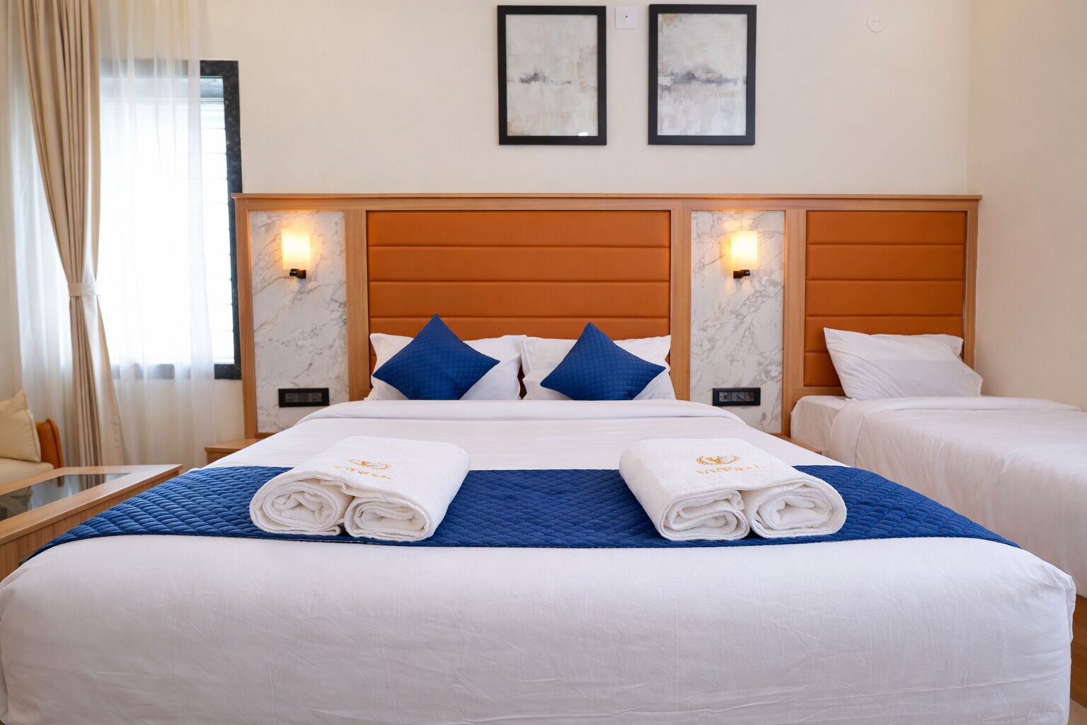 Quarto de hotel com uma cama grande, duas mesas de cabeceira, um criado-mudo de mármore e um aplique na parede.