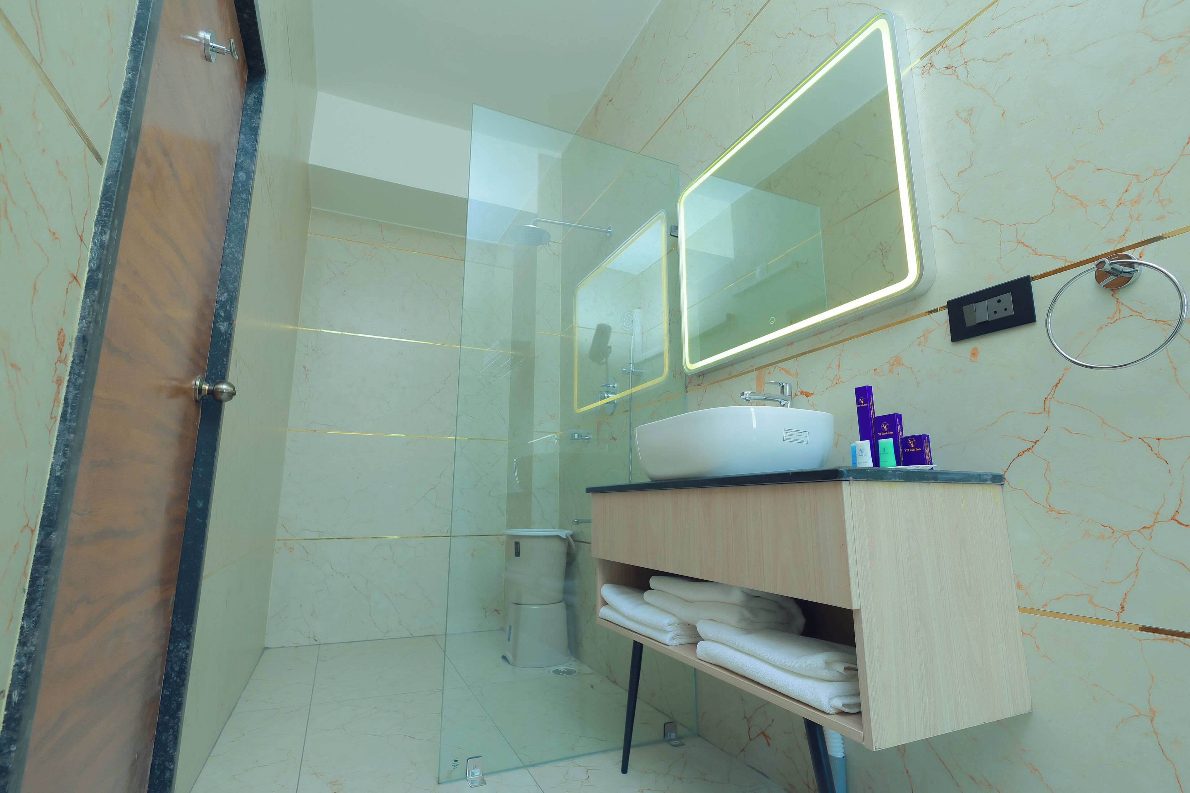 Une salle de bain moderne avec une douche à parois de verre, un meuble-lavabo en bois avec un miroir et un mur décoré d’un motif imitant le marbre.