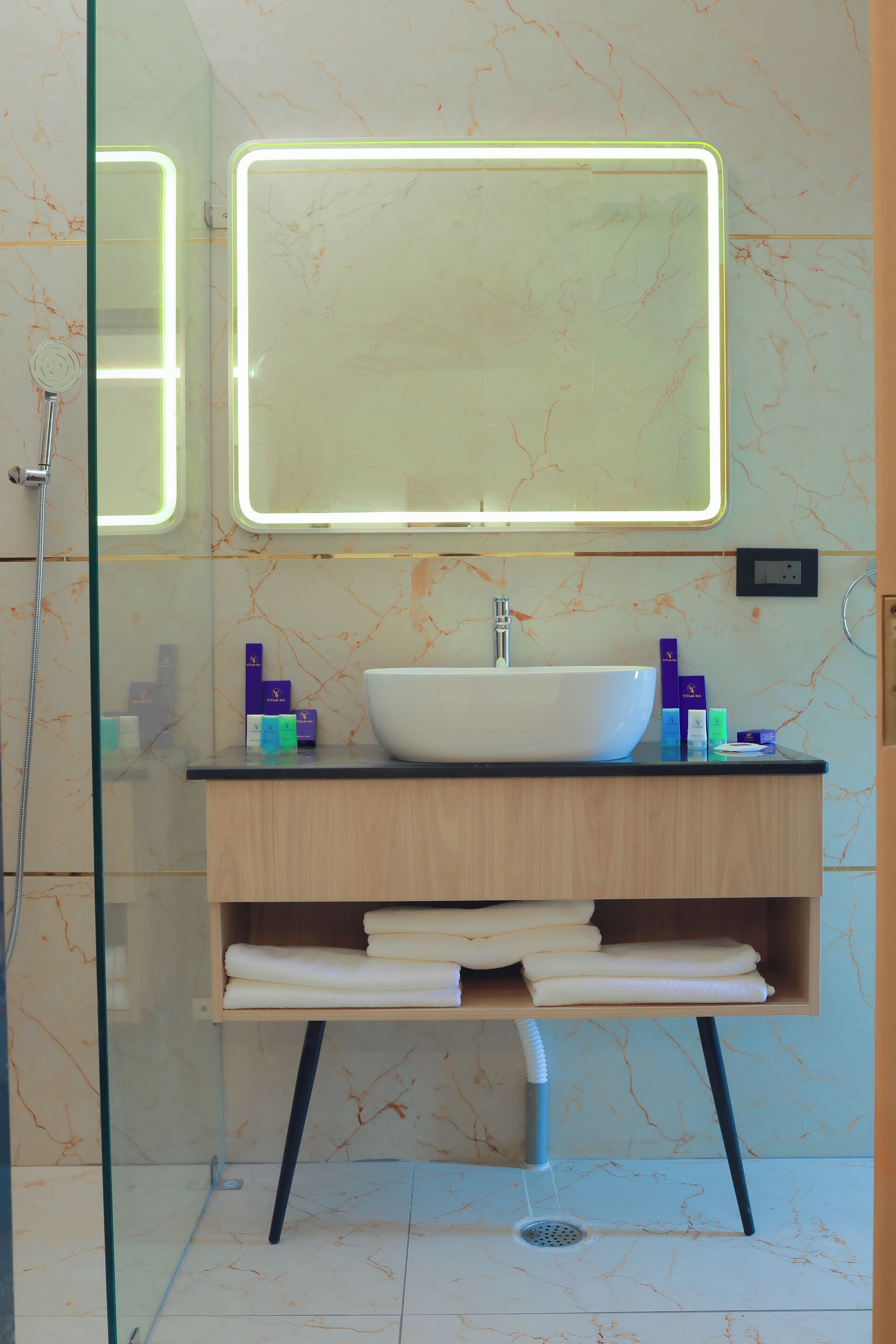 A bathroom with a glass-enclosed shower, a white sink, and a mirror with a lighted frame.