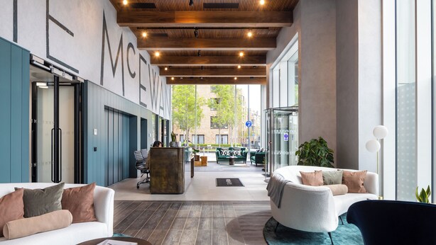 En modern hotellobby med ett träbeklätt tak, stora fönster, sittgrupper och en receptionsdisk.