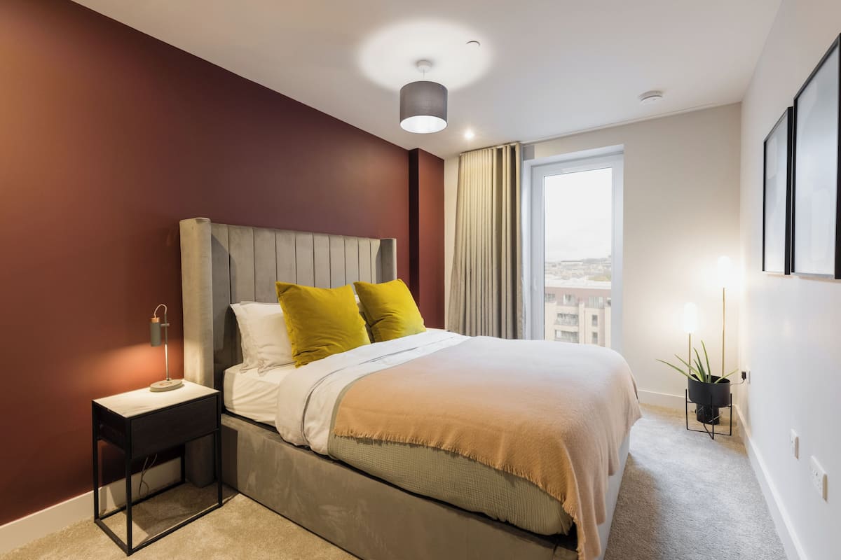 A modern bedroom with a bed, bedside table, lamp, and a potted plant.