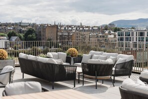 A rooftop terrace with outdoor furniture, a view of a cityscape, and a railing. - The McEwan (Edinburgh)