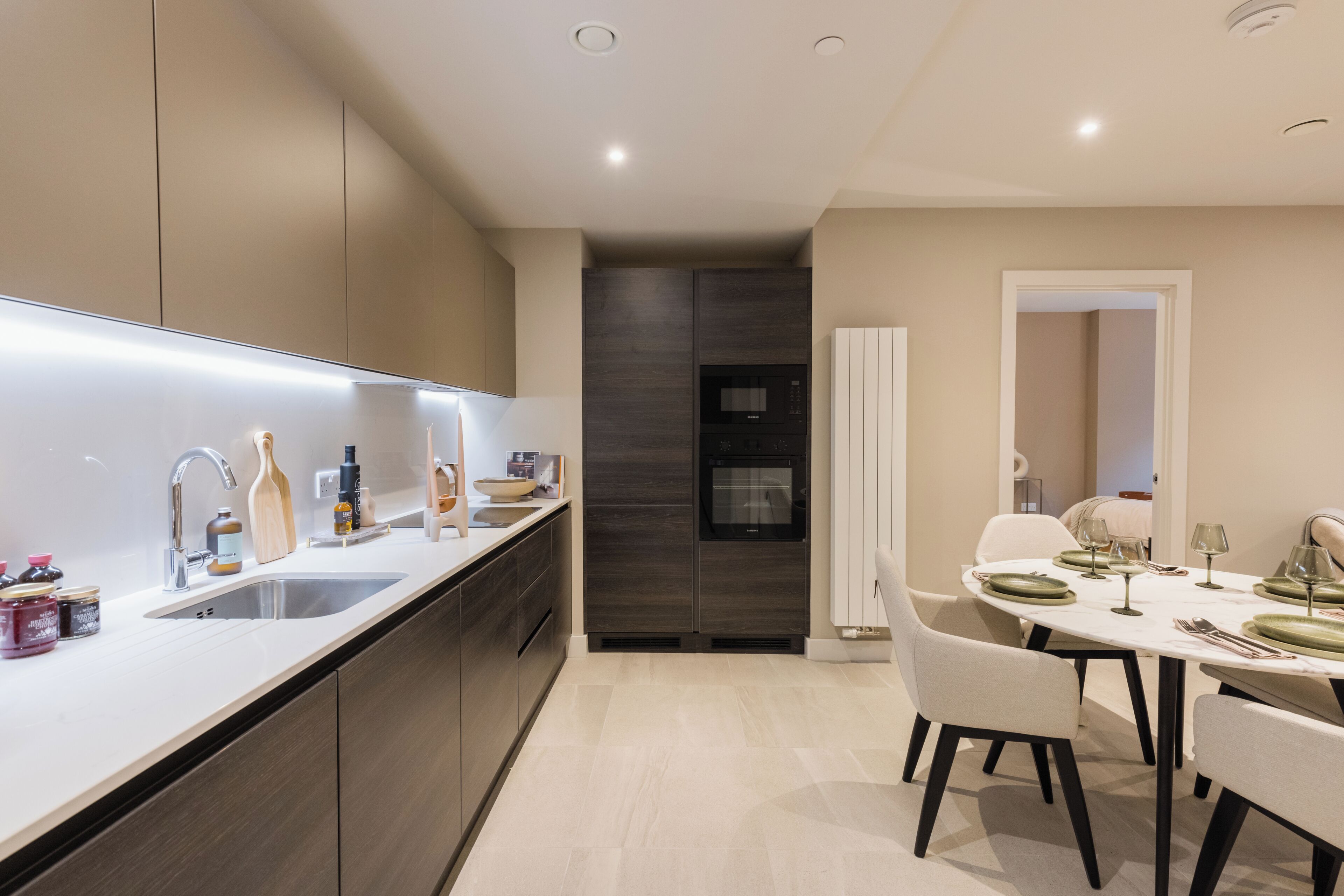 Une cuisine moderne dotée d’un four encastré, un coin repas avec une table dressée pour quatre personnes, et une salle à manger séparée avec une chaise.