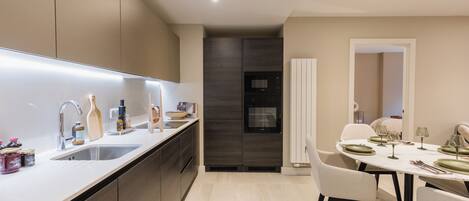 Une cuisine moderne dotée d’un four encastré, un coin repas avec une table dressée pour quatre personnes, et une salle à manger séparée avec une chaise.