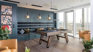 Ett modernt loungeområde med ett biljardbord, sittplatser och stora fönster.
