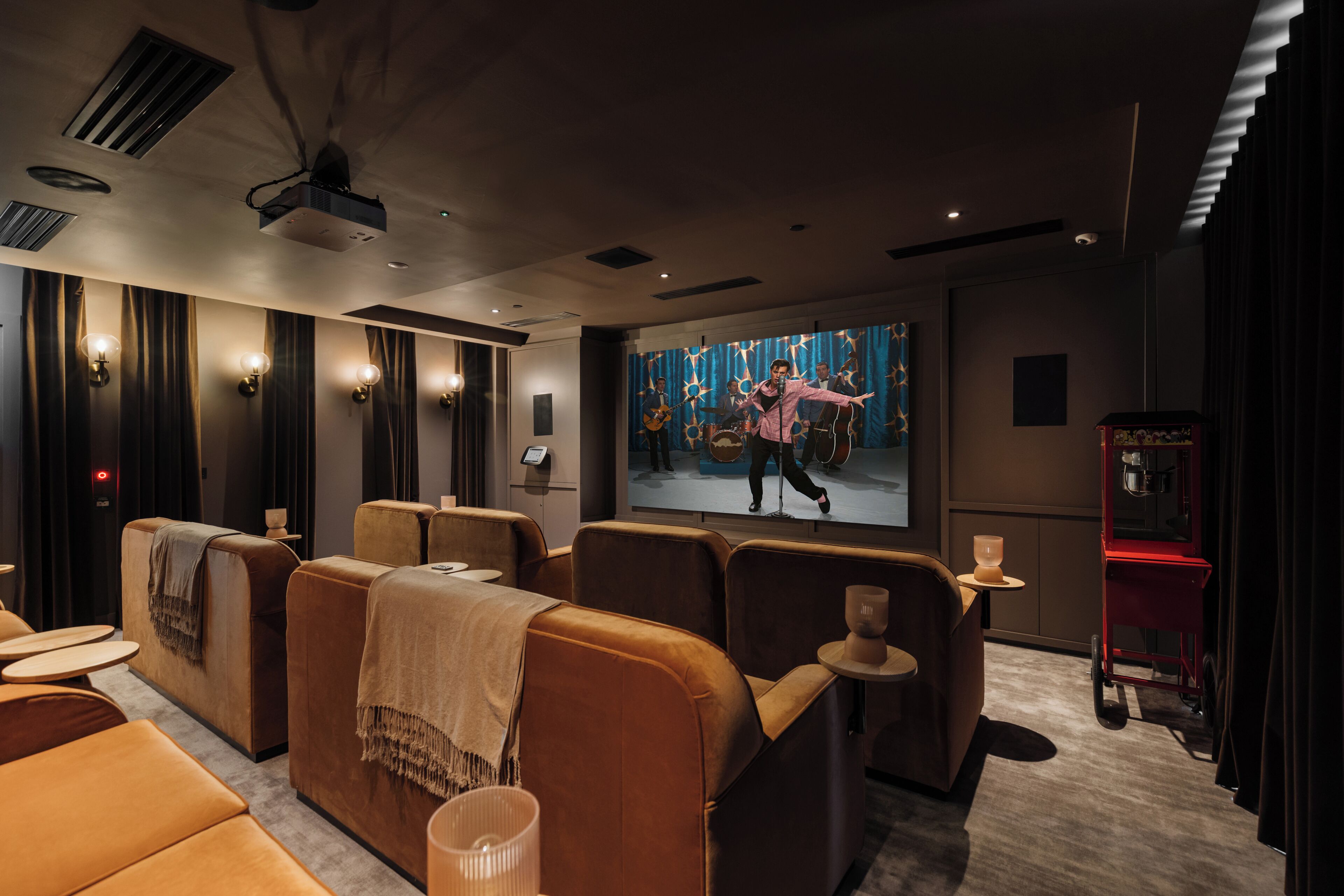 A modern cinema room with plush seating, a large screen, and a red coffee machine.