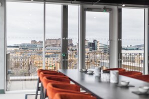 A dining area with a table and chairs, large windows with a city view, and a modern interior design. - The McEwan (Edinburgh)