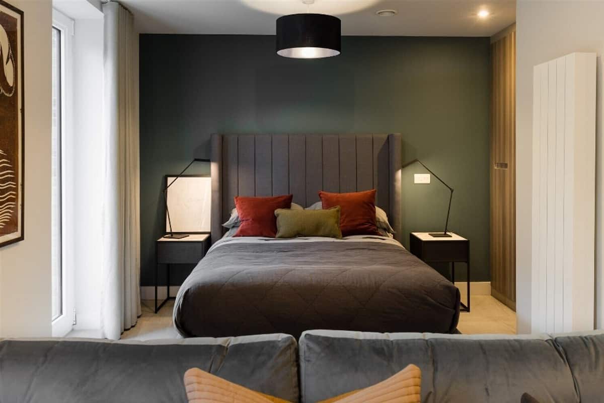 A modern bedroom with a large bed, bedside lamps, a headboard, and a view of the outside.