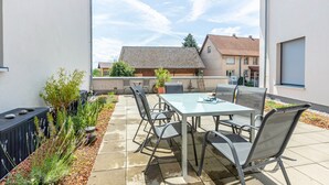 Eine Terrassengruppe mit Tisch und Stühlen, umgeben von Pflanzen und einem schwarzen Zaun.