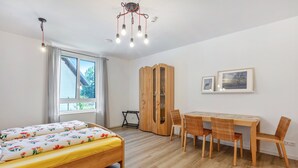 Ein Zimmer mit einem Bett, einem Esstisch mit Stühlen, einem Kleiderschrank und einer Deckenleuchte.