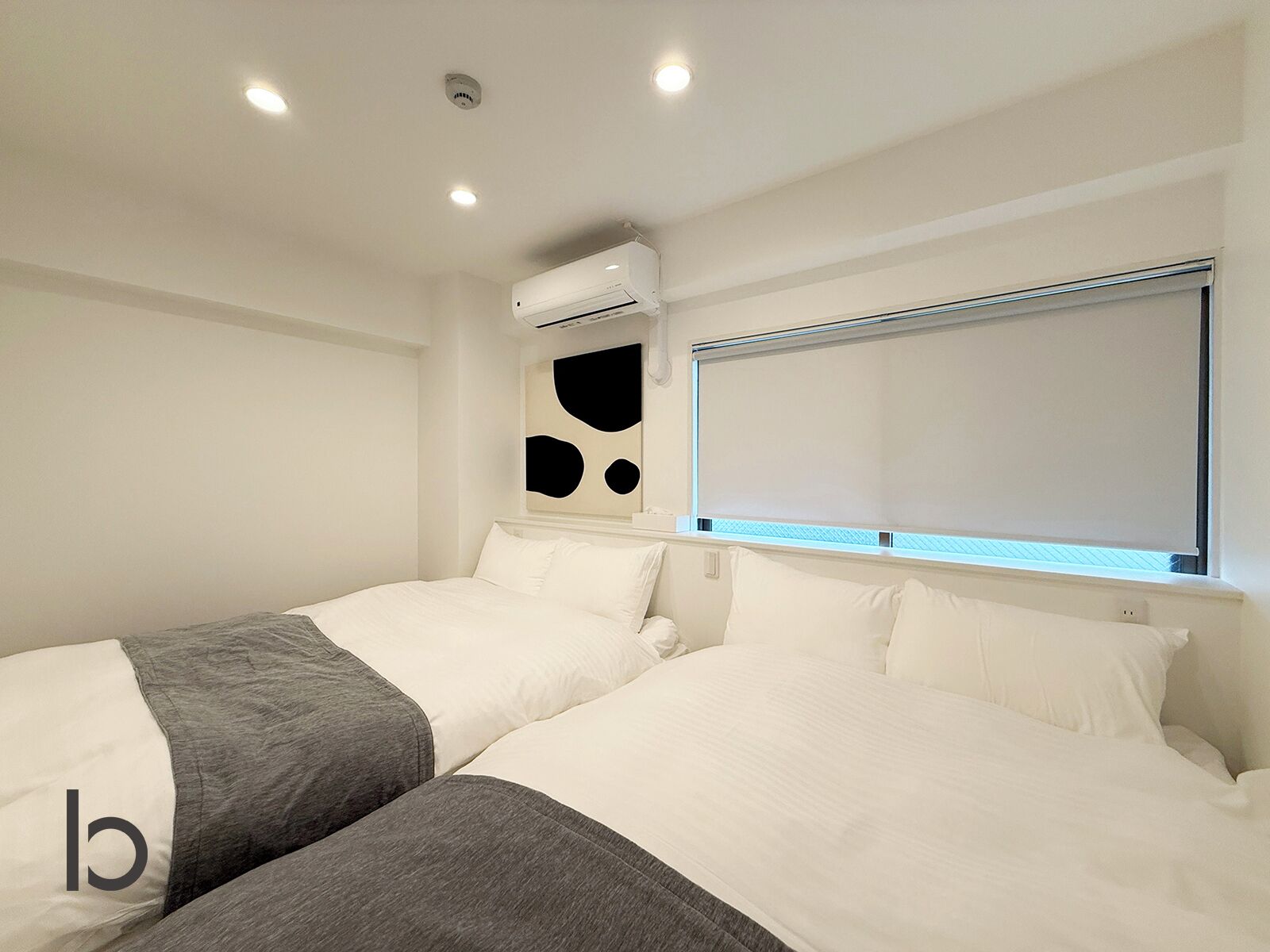 A hotel room with two beds, a window with blinds, an air conditioning unit, and a ceiling light.