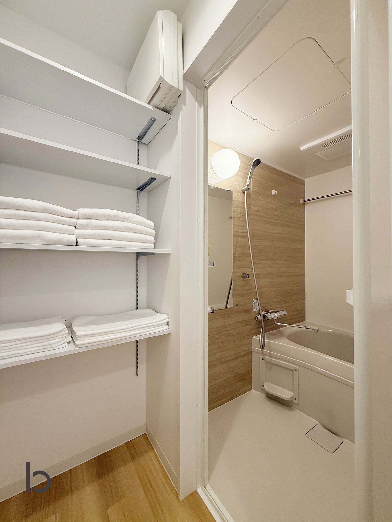 A bathroom with a shower, toilet, and shelves with folded towels.