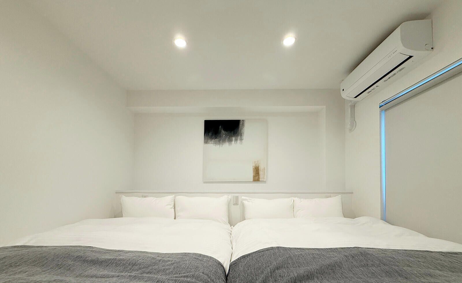 A modern hotel room with a large bed, a wall-mounted air conditioner, and a ceiling light.