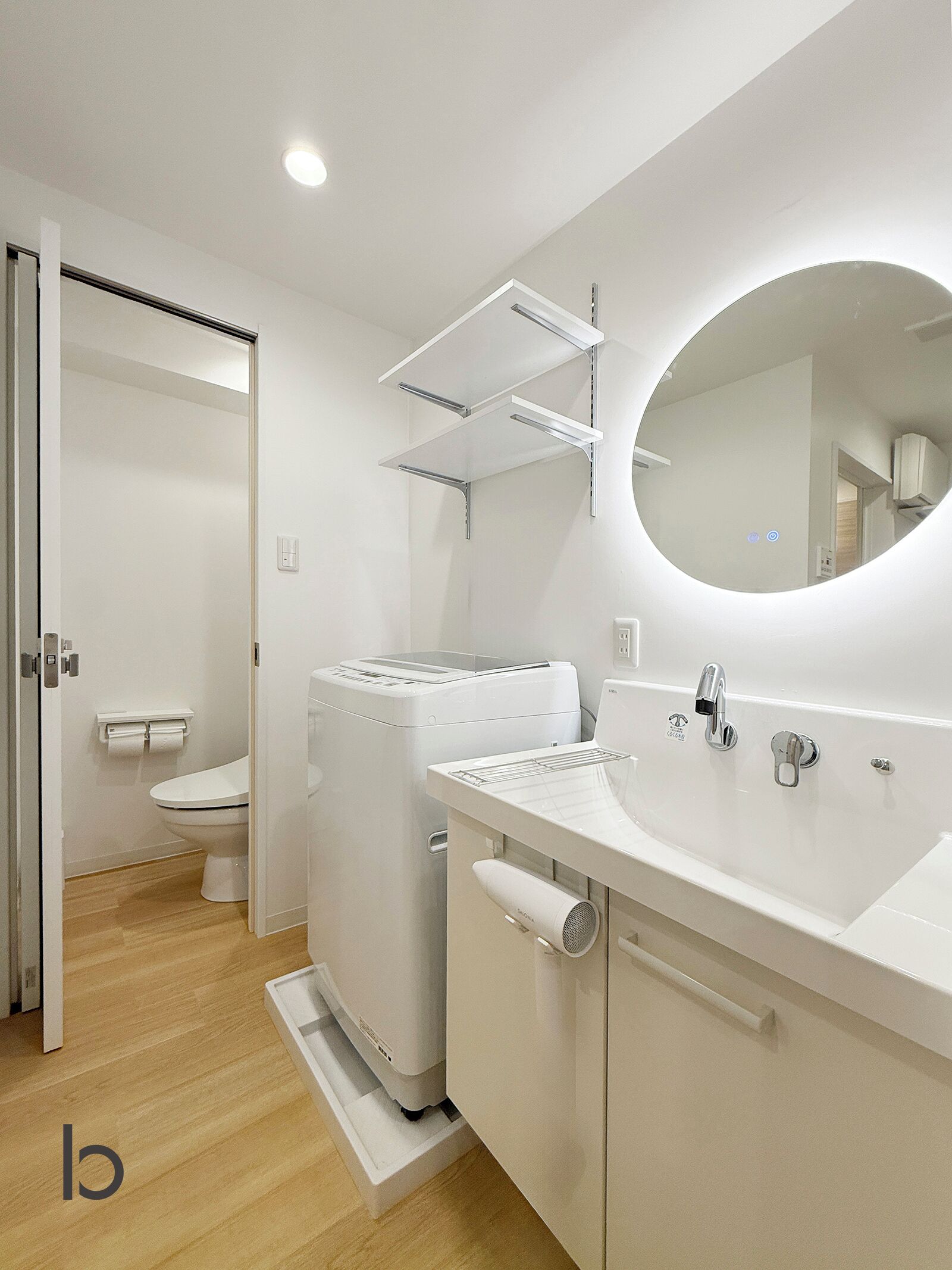 Une salle de bain moderne équipée de toilettes, d’un lave-linge, d’un lavabo et d’un miroir.