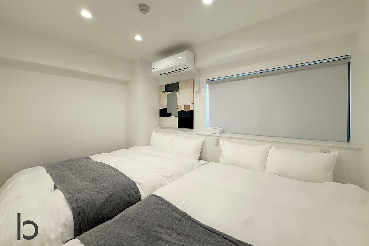 Una habitación de hotel moderna con una cama grande, un equipo de aire acondicionado, una ventana con persianas y un espejo montado.
