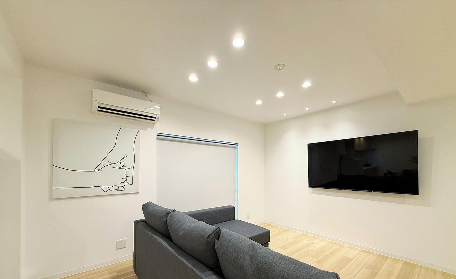 A modern living room with a grey sofa, a mounted flat-screen TV, and a piece of abstract art on the wall.