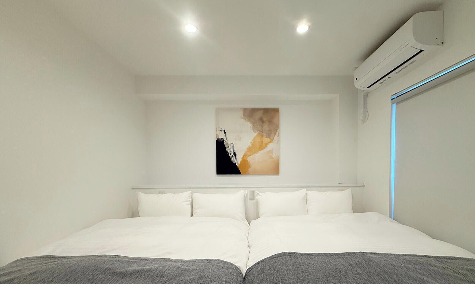 A modern hotel room with a large bed, white walls, and a ceiling-mounted air conditioner.