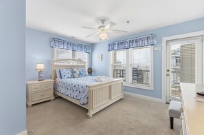 A bedroom with a bed, bedside tables, a ceiling fan, and large windows with blinds. - Big Blue - Second Row Home with Ocean Views! (Carolina Beach)