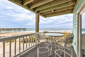 A covered outdoor area with a table and chairs, overlooking a beach with a pier. - A3 Island North - Carolina Beach - Ocean Views & Community Pool l Sleeps 7 (Carolina Beach)