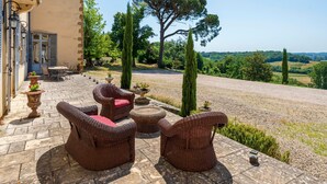 Un patio con muebles de mimbre, una mesa y sillas, con vista a un paisaje rural con árboles y cielo despejado.