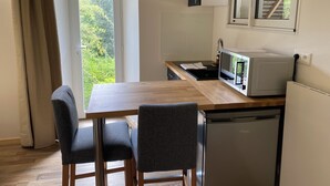 Een kleine keuken met een houten tafel, twee stoelen, een magnetron en een koelkast.