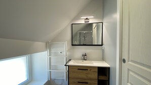 Een moderne badkamer met een wit wastafelmeubel, een spiegel, een handdoekrek en een raam.
