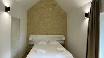 Een slaapkamer met een schuine plafond, een bed met witte lakens, een houten tafel en een stoel.