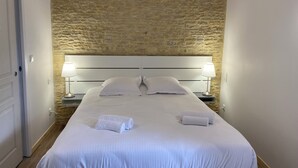 Een hotelkamer met een stenen muur, een groot bed met witte lakens, twee bedlampen en een deur.