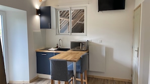 Een kleine keuken met een magnetron, spoelbak en een houten tafel.
