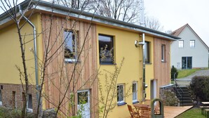 A modern house with a yellow facade, a wooden deck, and a stone fireplace. - Feriendomizil XXL auf der Insel Poel Nahe Strand (Insel Poel)