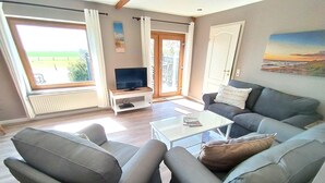 Una sala de estar con un sofá, sillones, una mesa de centro, un televisor sobre un mueble bajo y un cuadro en la pared.