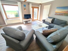 Una sala de estar con un sofá, sillones, una mesa de centro, un televisor sobre un mueble bajo y un cuadro en la pared.