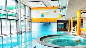 Una piscina interior con paredes de vidrio transparente, un jacuzzi y un mural colorido en la pared.