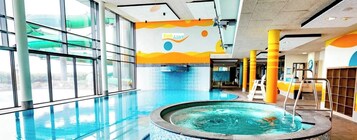 Una piscina interior con paredes de vidrio transparente, un jacuzzi y un mural colorido en la pared.
