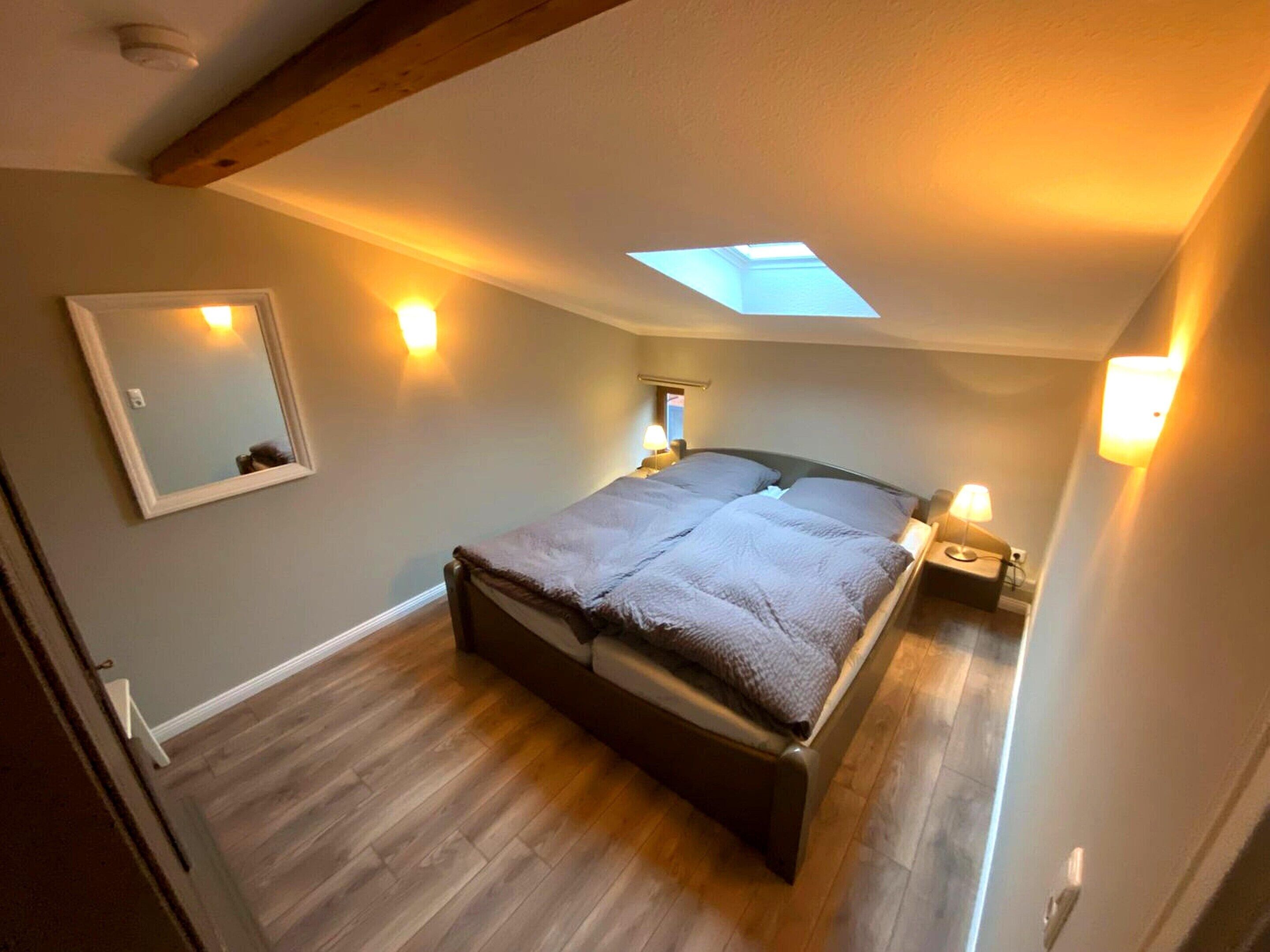 Een slaapkamer met dakraam, een bed, nachtlampjes en een spiegel.