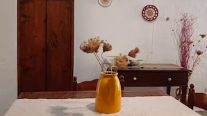 Una mesa de madera con un jarrón amarillo y flores secas, un aparador de madera y una pared decorada con platos.
