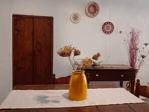 Un tavolo in legno con un vaso giallo e fiori secchi, un mobiletto in legno e una parete con piatti decorativi.
