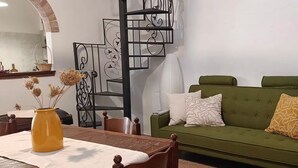 Un salón con un sofá verde, una mesa de comedor de madera y un jarrón amarillo con flores secas.