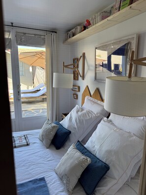 A hotel room with a bed, pillows, a bedside table, a lamp, a mirror, and a window with curtains. - Charming villa 'Le Refuge' heated pool 300m from the beach in a quiet location (La Tranche-sur-Mer)