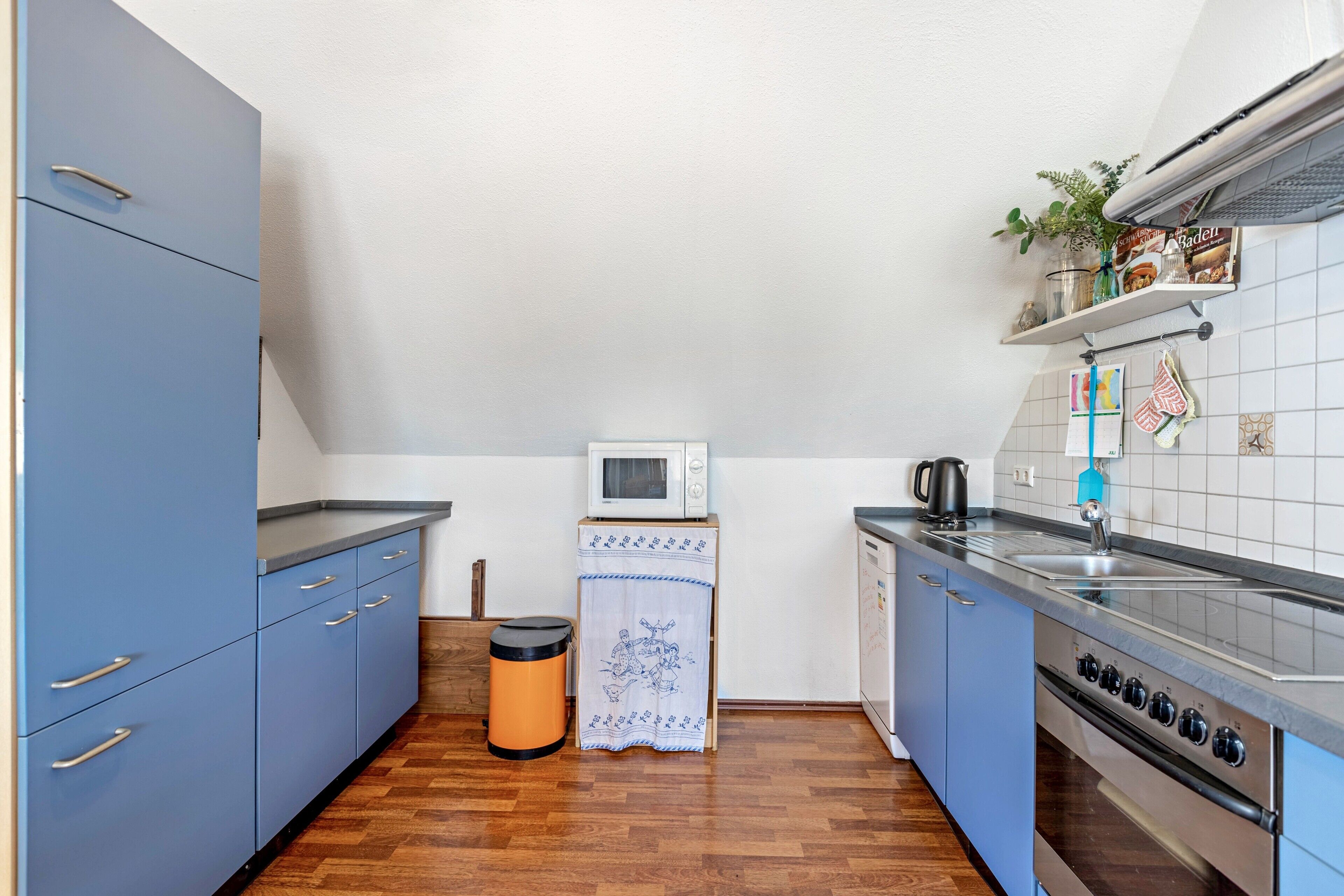 A compact kitchen with blue cabinets, a microwave, a kettle, and a stove.