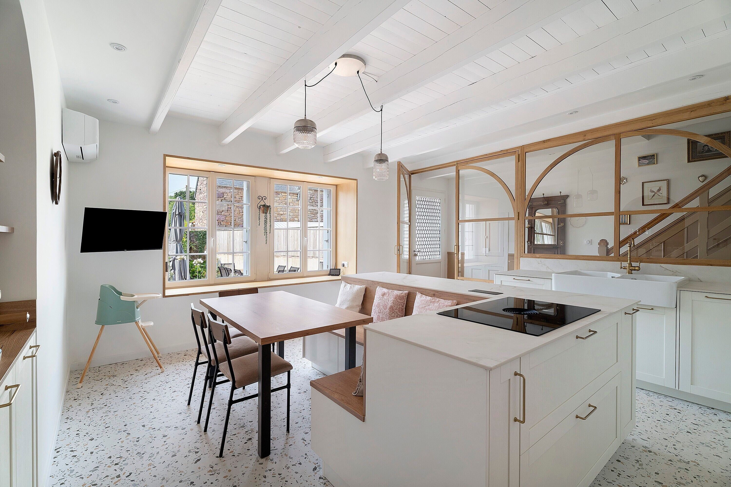 A modern kitchen with a large island, wooden dining table, and a view of the outside.