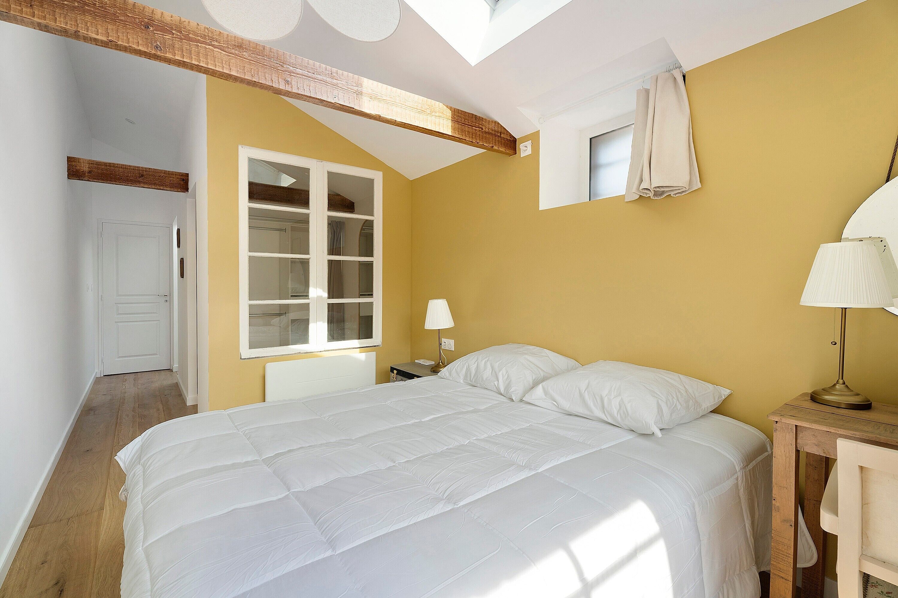 Ein Schlafzimmer mit einem Bett, einem Nachttisch, einer Lampe, einem Fenster und einer Tür.