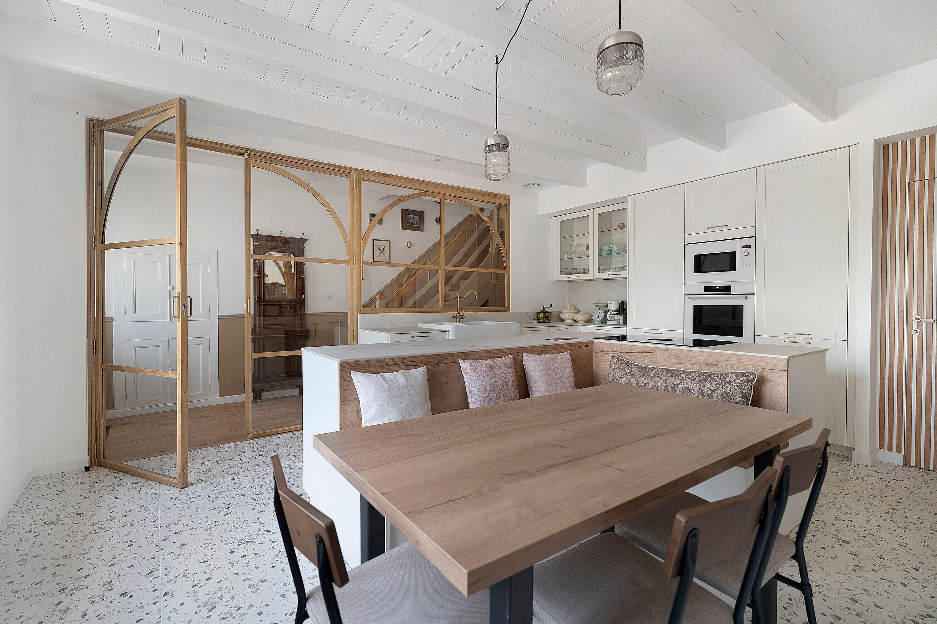 A modern kitchen with white cabinetry, a wooden dining table, and a staircase leading to another level.