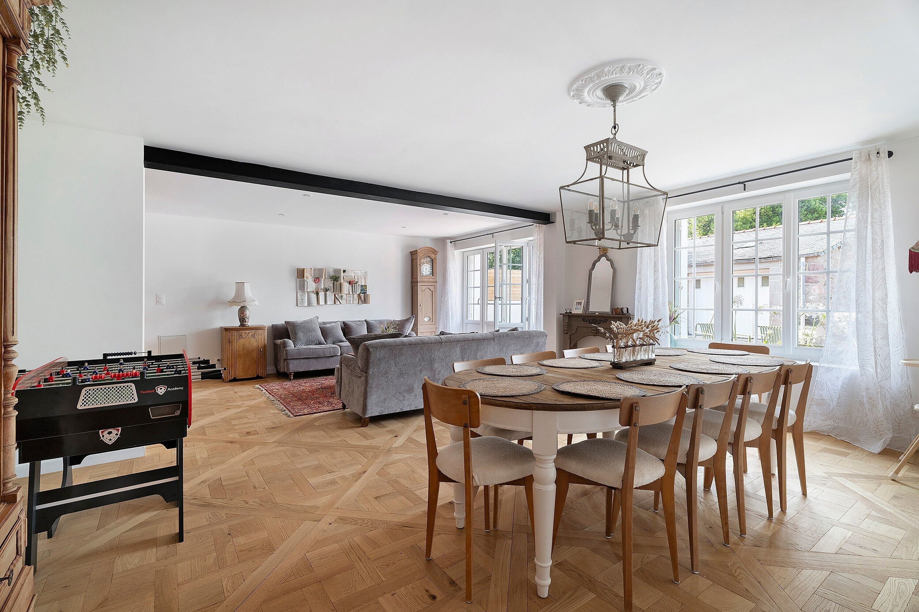 A dining area with a round table, wooden chairs, and a foosball table.
